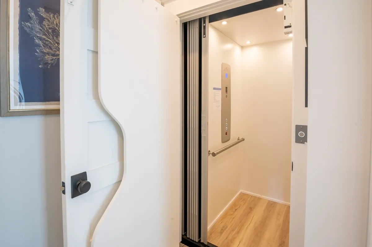 This interior image features a modern elevator door with sleek controls, wooden flooring, and decorative wall art, presenting a contemporary and accessible environment within the home.