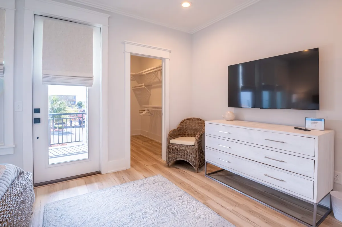 A comfortable bedroom featuring a large TV, white dresser, and a door leading directly to a balcony. The setup encourages both relaxation and easy access to the outdoors, perfect for starting mornings with coffee or winding down after an adventure.