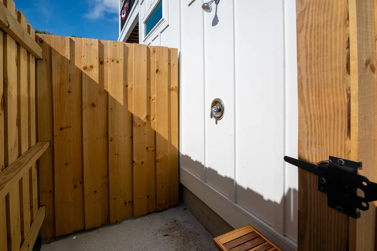 An intimate view of the outdoor shower area, featuring a wooden fence, a clean shower fixture, and a small bench. Sunlight streaming in adds a refreshing, rejuvenating feel to the scene.