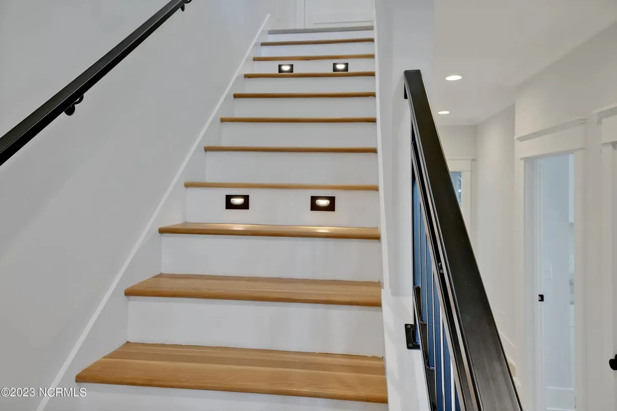 The image shows a warmly lit staircase with attractive lighting fixtures and a sturdy handrail. The scene captures an inviting sense of arrival, with the possibility of seasonal decorations or family gatherings in the shared space, subtly hinting at the anticipation of a new experience at Blue Pearl.