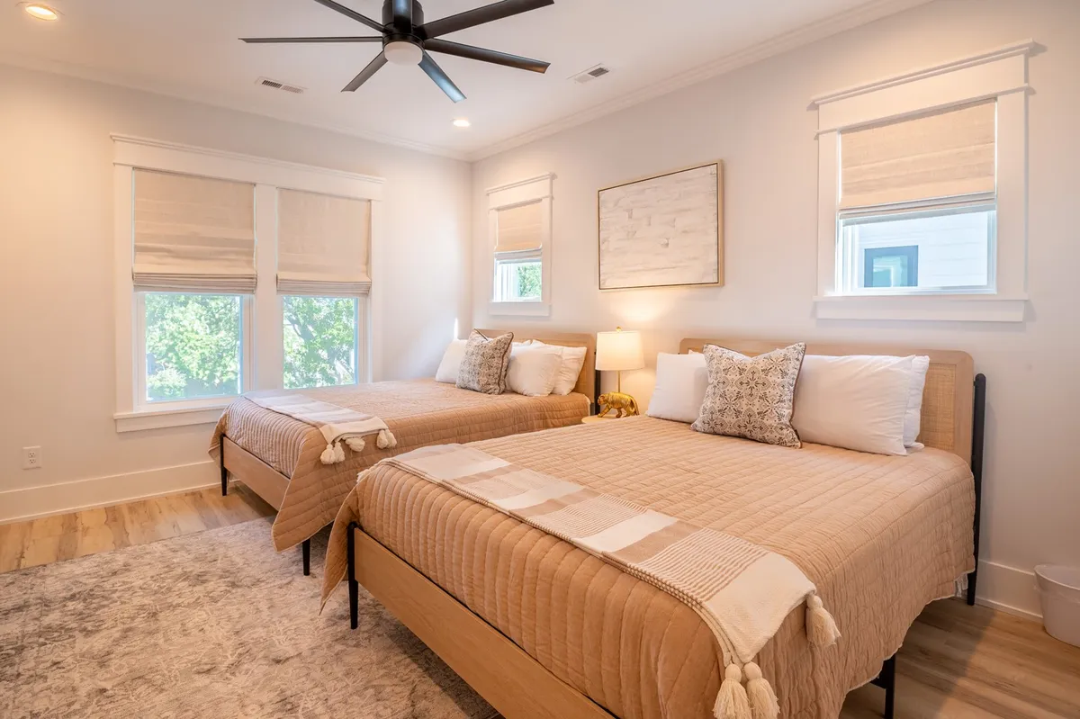 A calm, inviting bedroom featuring two beds with decorative pillows, a bedside lamp, and artwork on the wall. The space is well-lit and designed for relaxation or socializing, making it ideal for families or guests.