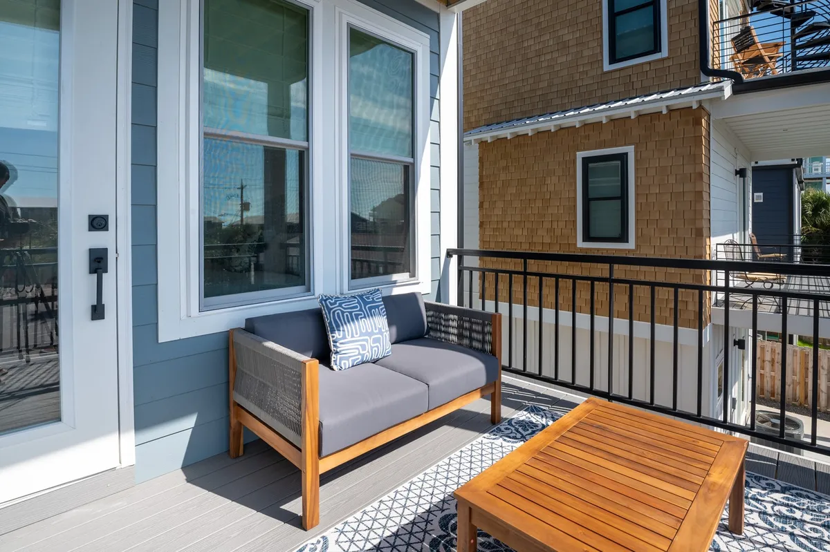 An inviting outdoor seating area featuring a gray sofa with a decorative pillow and a wooden coffee table, set against a serene backdrop. The space is designed for relaxation and socializing, with the view extending outwards, possibly hinting at coastal surroundings.