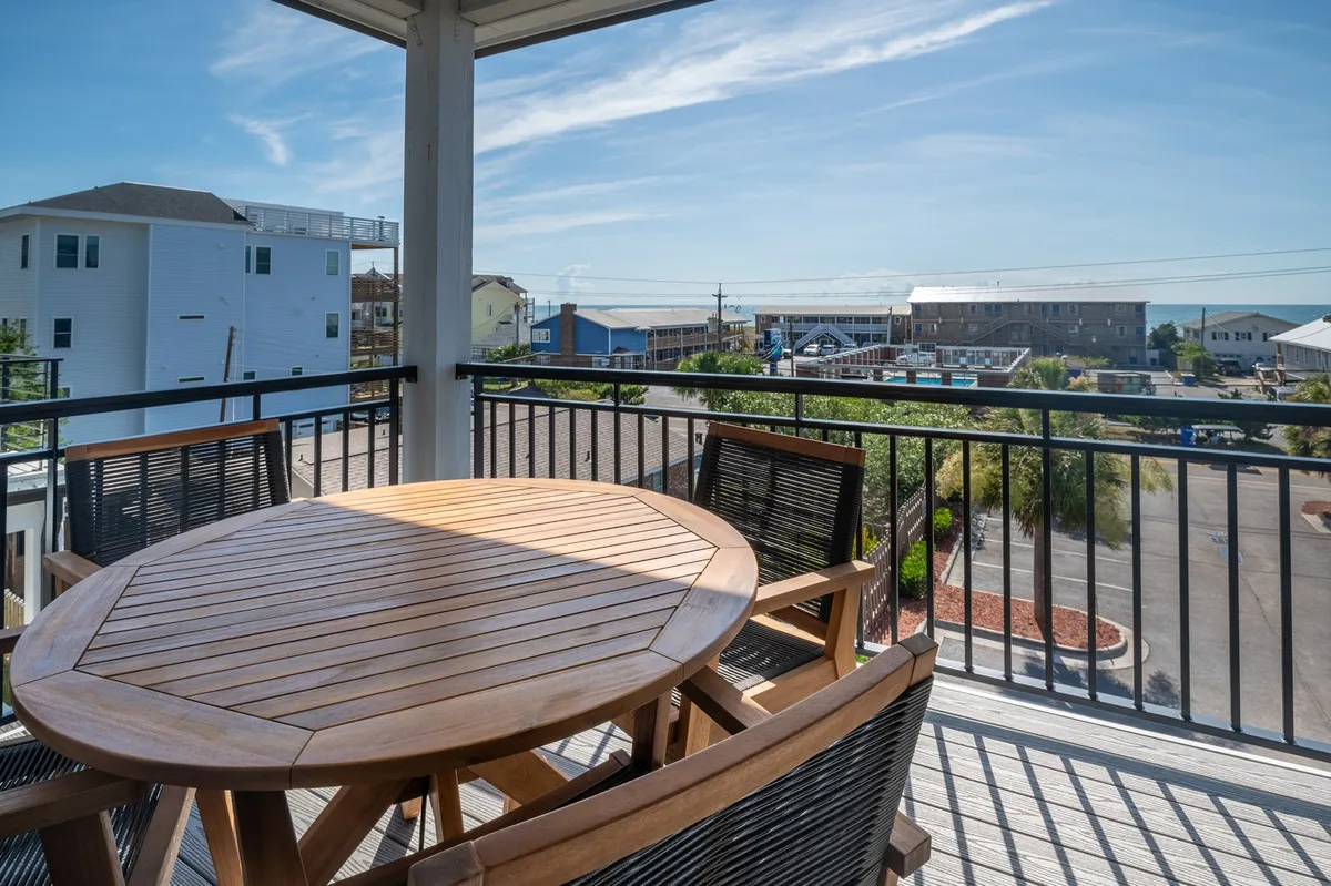 A spacious outdoor dining area featuring a wooden table and comfortable chairs, set on a porch or patio with an open view of the surrounding neighborhood. The setting is perfect for al fresco meals, family game nights, or evening conversations under the stars.