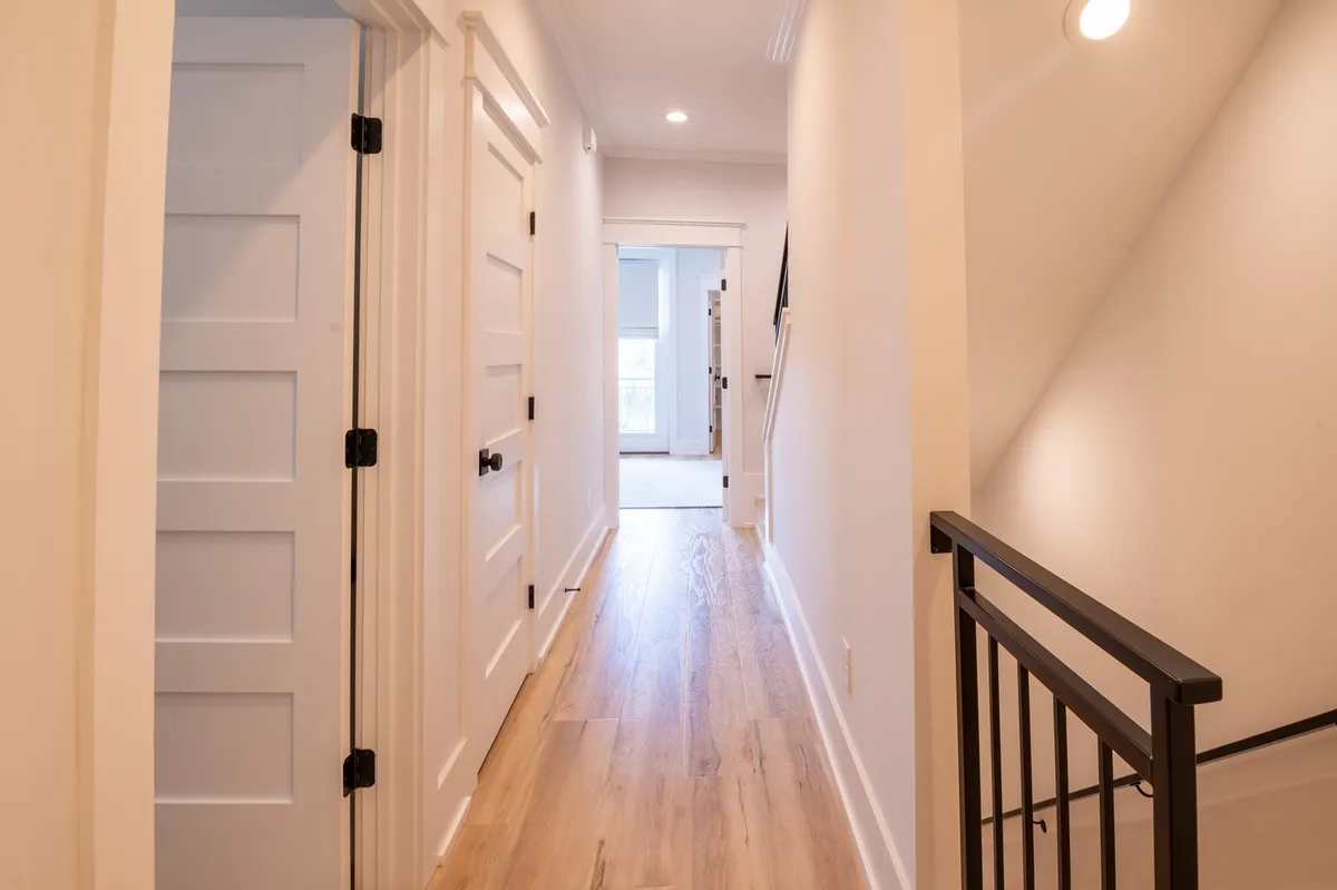 A bright, inviting hallway with wooden flooring and white walls, featuring door frames and a staircase leading to other rooms. The open layout offers a sense of flow, suggesting easy transitions between indoor spaces and the outside world.