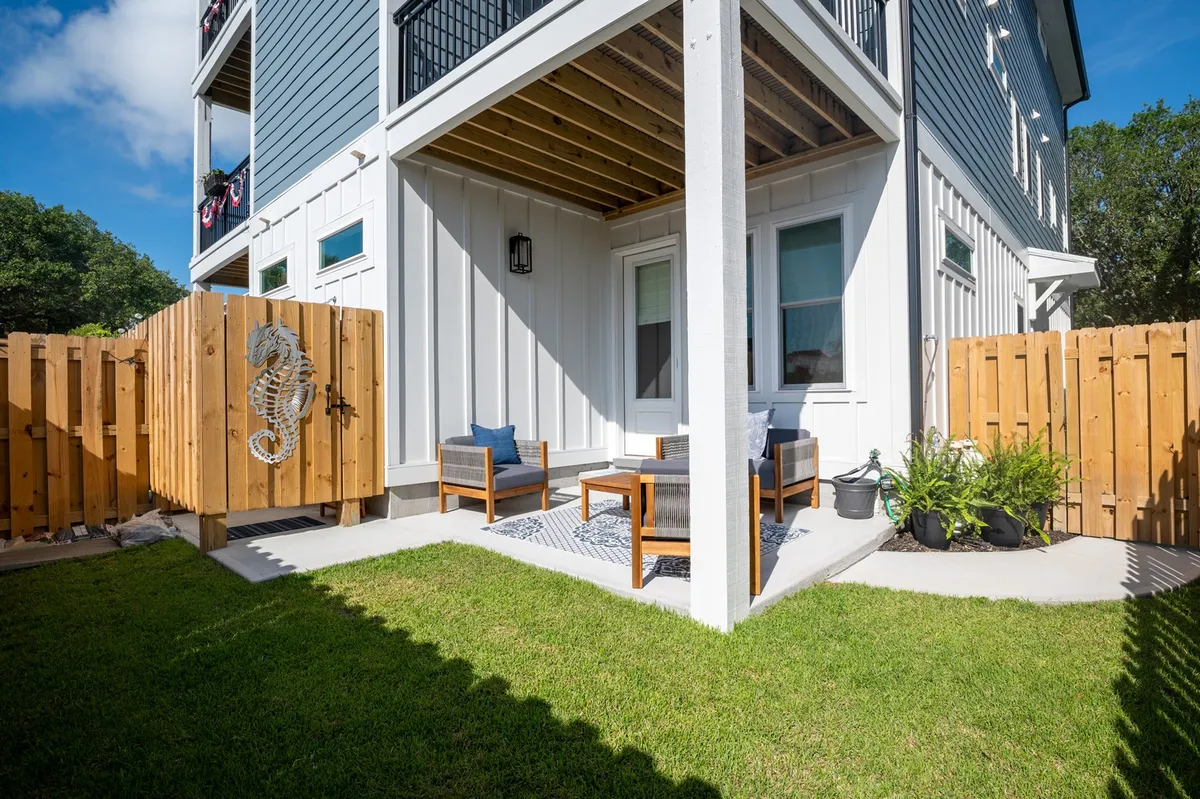 An exterior view of a wooden gate adorned with a seahorse design, opening to an outdoor seating area with plush blue cushions and a patterned rug. The setup suggests a welcoming, playful environment ideal for both adults and kids.