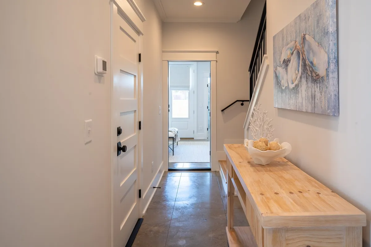 An inviting entryway featuring a table, ocean-themed artwork, staircase, and a doorway leading into the home, all filled with natural light.